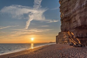 A coastal sunset with a rocky cliff and a beach. - Cosy Holiday Home at Freshwater Beach Holiday Park on the iconic Jurassic Coast (Bridport)