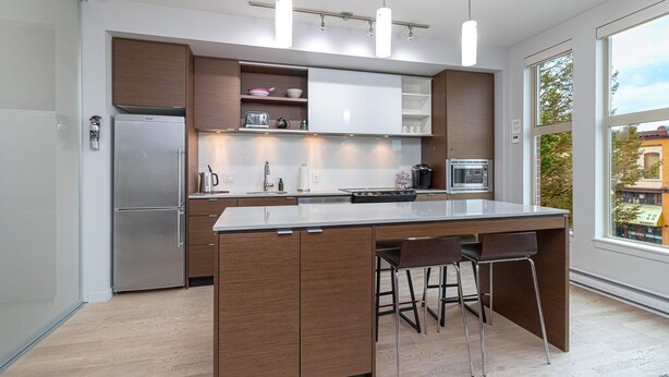 A modern kitchen with a central island, stainless steel appliances, and wooden cabinetry. - Sleek Kitchen Island and Garden Views (Victoria North)