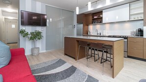 A modern kitchen with a central island, bar stools, a flat-screen TV, and a potted plant. - Sleek Kitchen Island and Garden Views (Victoria North)