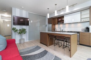 Eine moderne Küche mit einer zentralen Kochinsel, Barhocker, einem Flachbildfernseher und einem Blumentopf.
