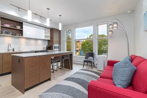 Eine moderne Küche mit einer zentralen Kochinsel, Barhocker und einem roten Sofa mit grauem Kissen.