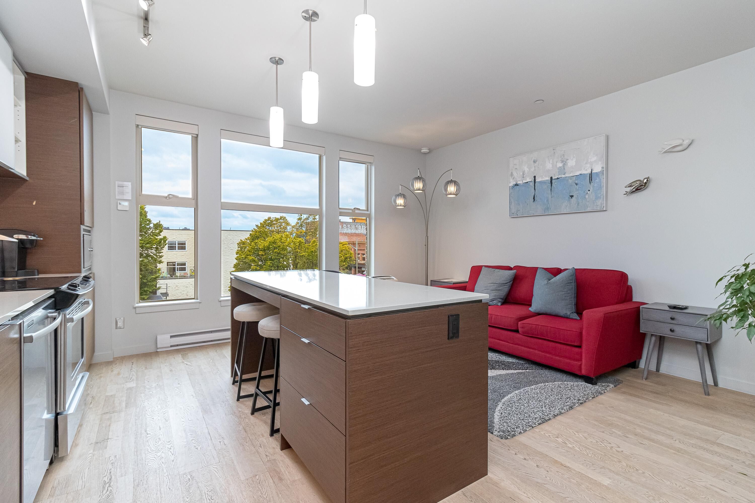 A modern kitchen with a central island, stainless steel appliances, and large windows offering a view of the outside.