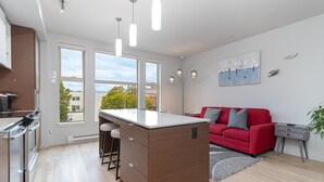 A modern kitchen with a central island, stainless steel appliances, and large windows offering a view of the outside. - Sleek Kitchen Island and Garden Views (Victoria North)
