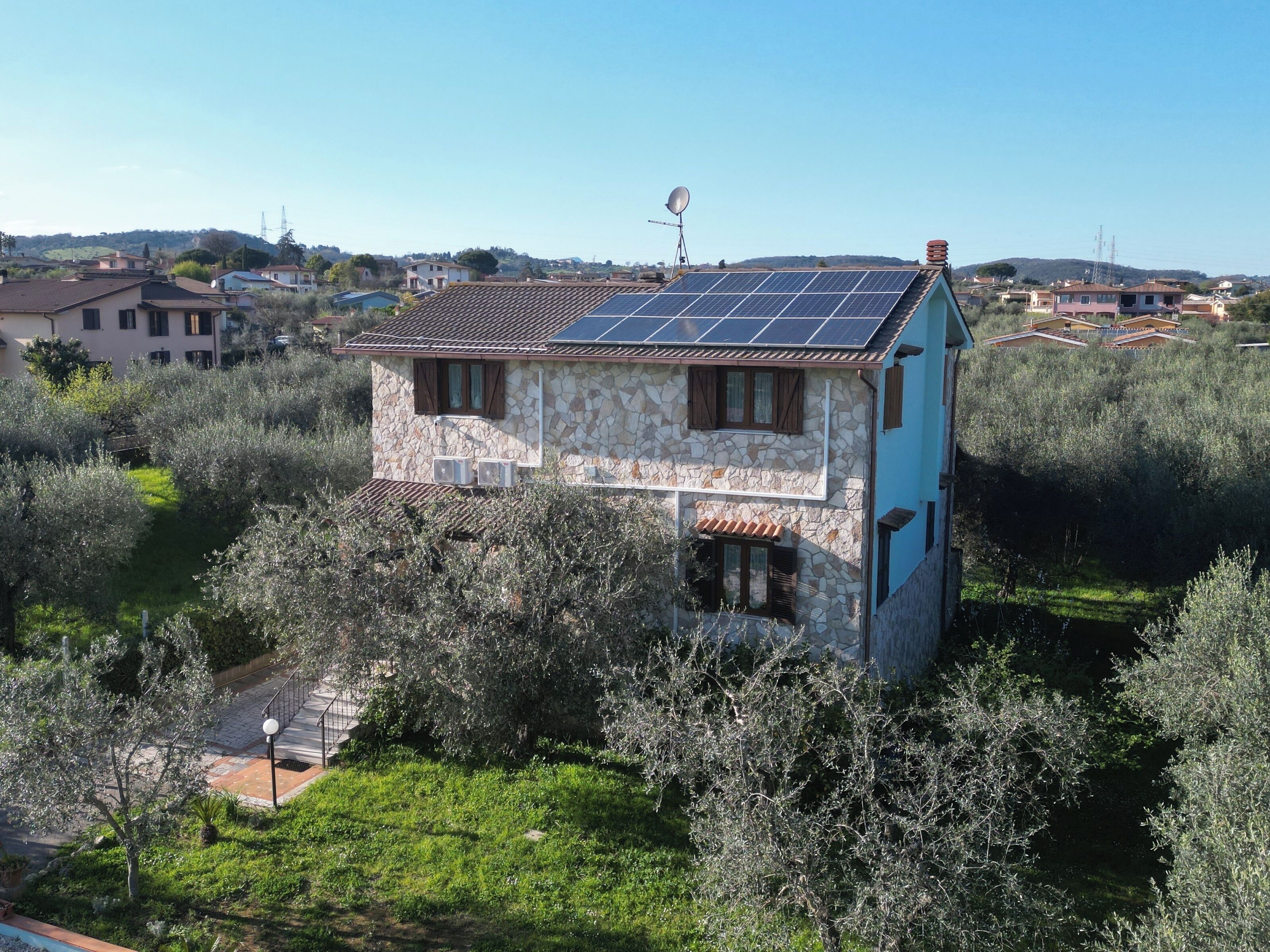 Una casa in pietra con pannelli solari sul tetto, immersa tra ulivi e un cielo sereno.