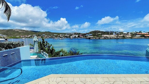 A swimming pool with a clear view of the sea and a distant town. - ☀️🌴Spinnaker 1312 by IRE Vacations - 2 bedroom Condo with Resort Amenities👙 (Oyster Pond)