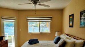 A bedroom with a bed, a ceiling fan, a window with a view of a body of water, and a wooden dresser. - ☀️🌴Spinnaker 1312 by IRE Vacations - 2 bedroom Condo with Resort Amenities👙 (Oyster Pond)