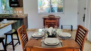 A dining area with a wooden table set for four, a kitchen in the background, and a window with a view of greenery. - ☀️🌴Spinnaker 1312 by IRE Vacations - 2 bedroom Condo with Resort Amenities👙 (Oyster Pond)