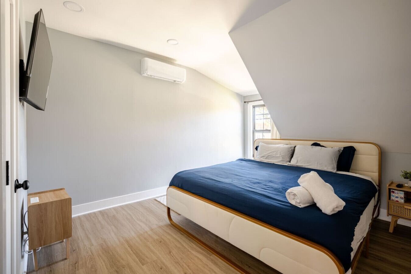 Ein Schlafzimmer mit einem Bett, einem an der Wand montierten Fernseher und einem kleinen Nachttisch.