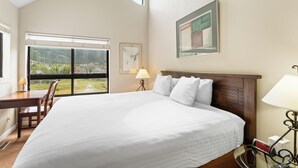 A hotel room with a large bed, a desk, a chair, a window with a view of greenery, and a framed picture on the wall. - Greens at Copper #318 By Summit County Mountain Retreats (Copper Mountain)
