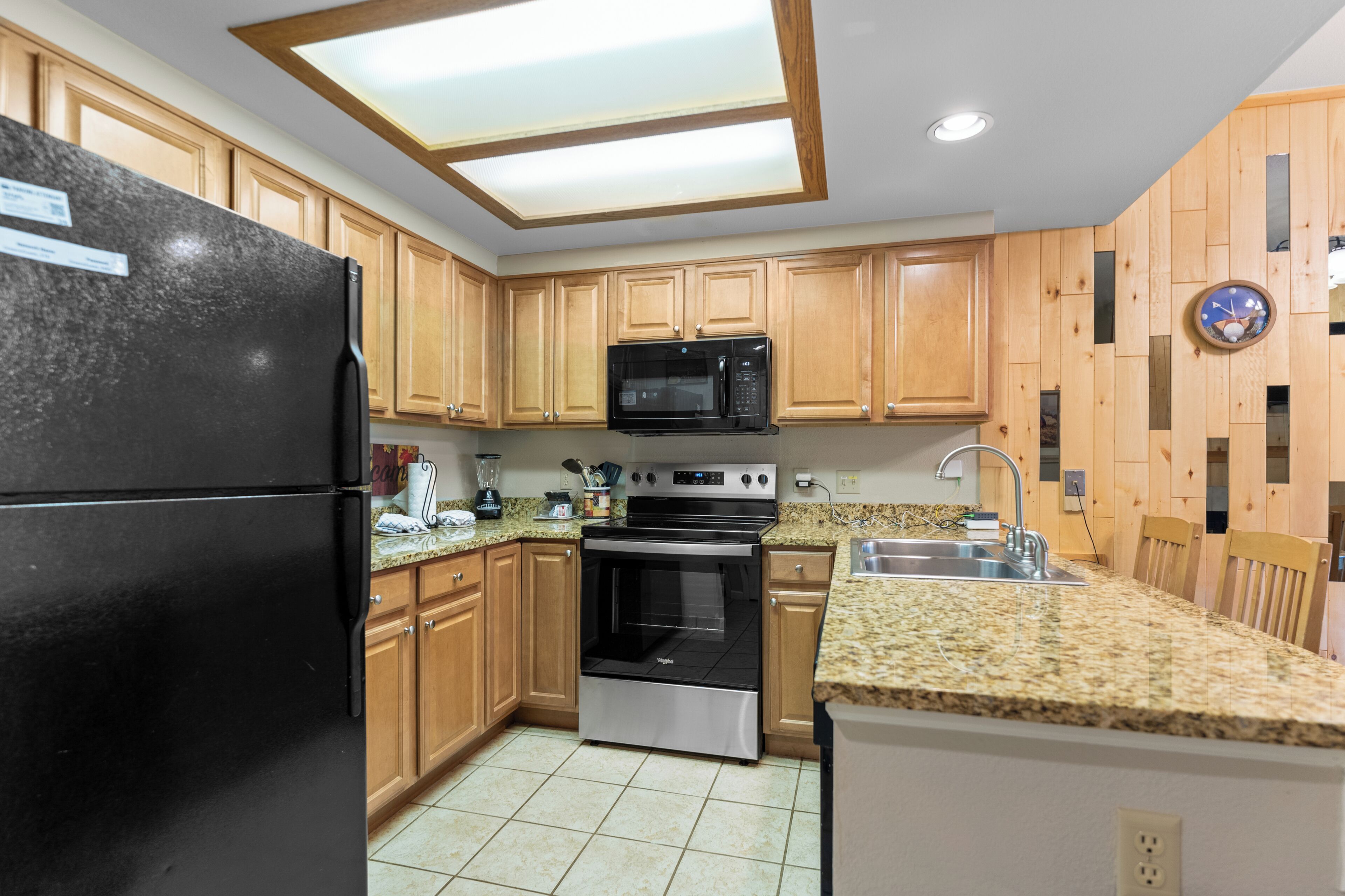Una cocina con armarios de madera, un refrigerador negro, microondas, horno y encimera de granito.