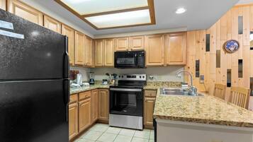Una cocina con armarios de madera, un refrigerador negro, microondas, horno y encimera de granito.