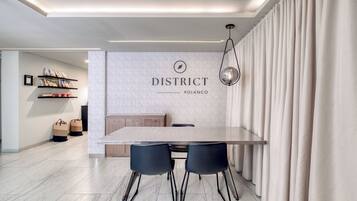 Un'area pranzo moderna con un tavolo lungo, due sedie nere, un mobiletto in legno e una parete con la scritta "DISTRICT POLANCO".