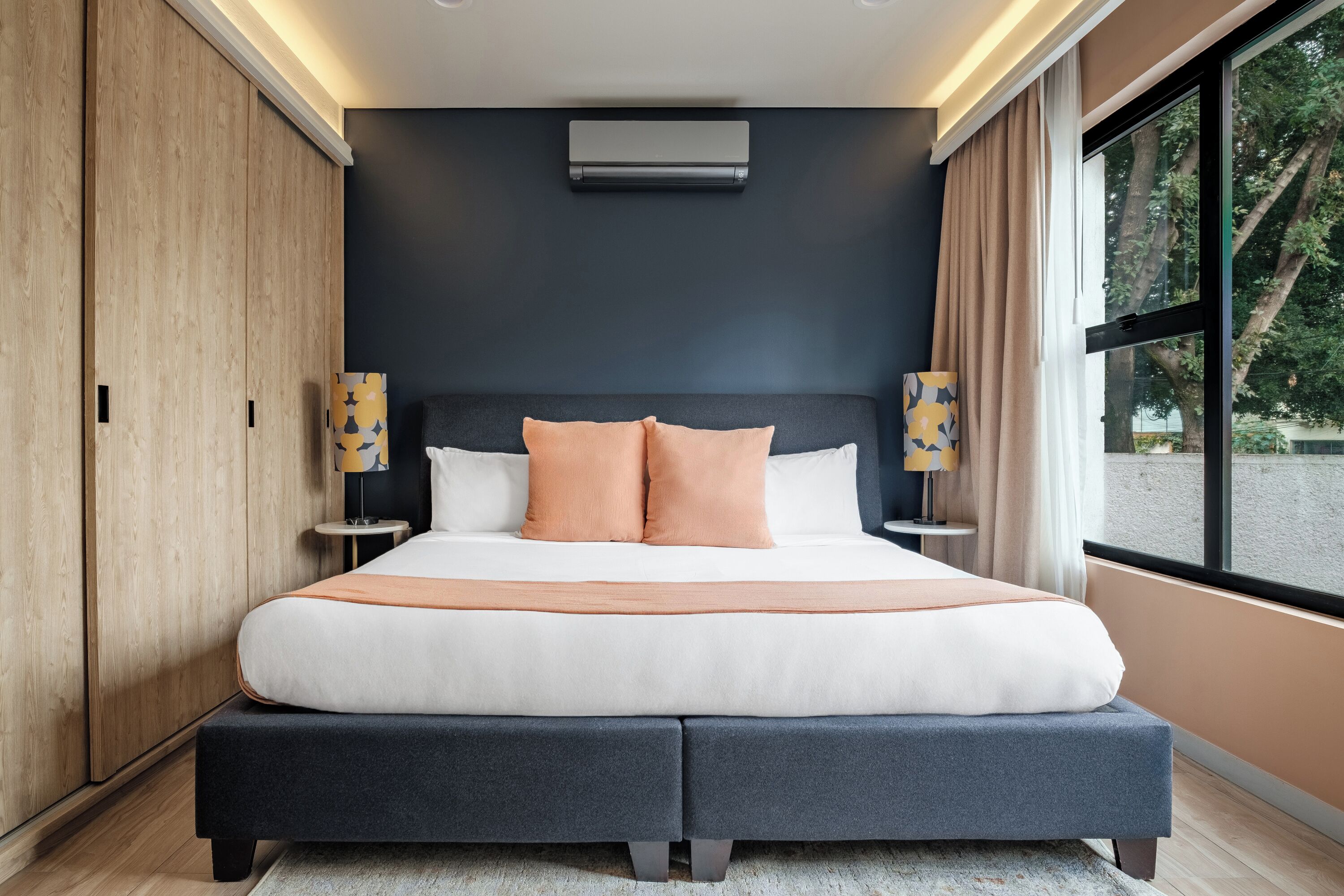 Una camera da letto moderna con un letto grande, pareti scure e una finestra con vista sugli alberi.
