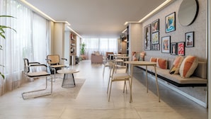 Una sala de estar moderna con un sofá, sillas, una mesa de centro y un comedor. Hay estanterías y obras de arte en las paredes.