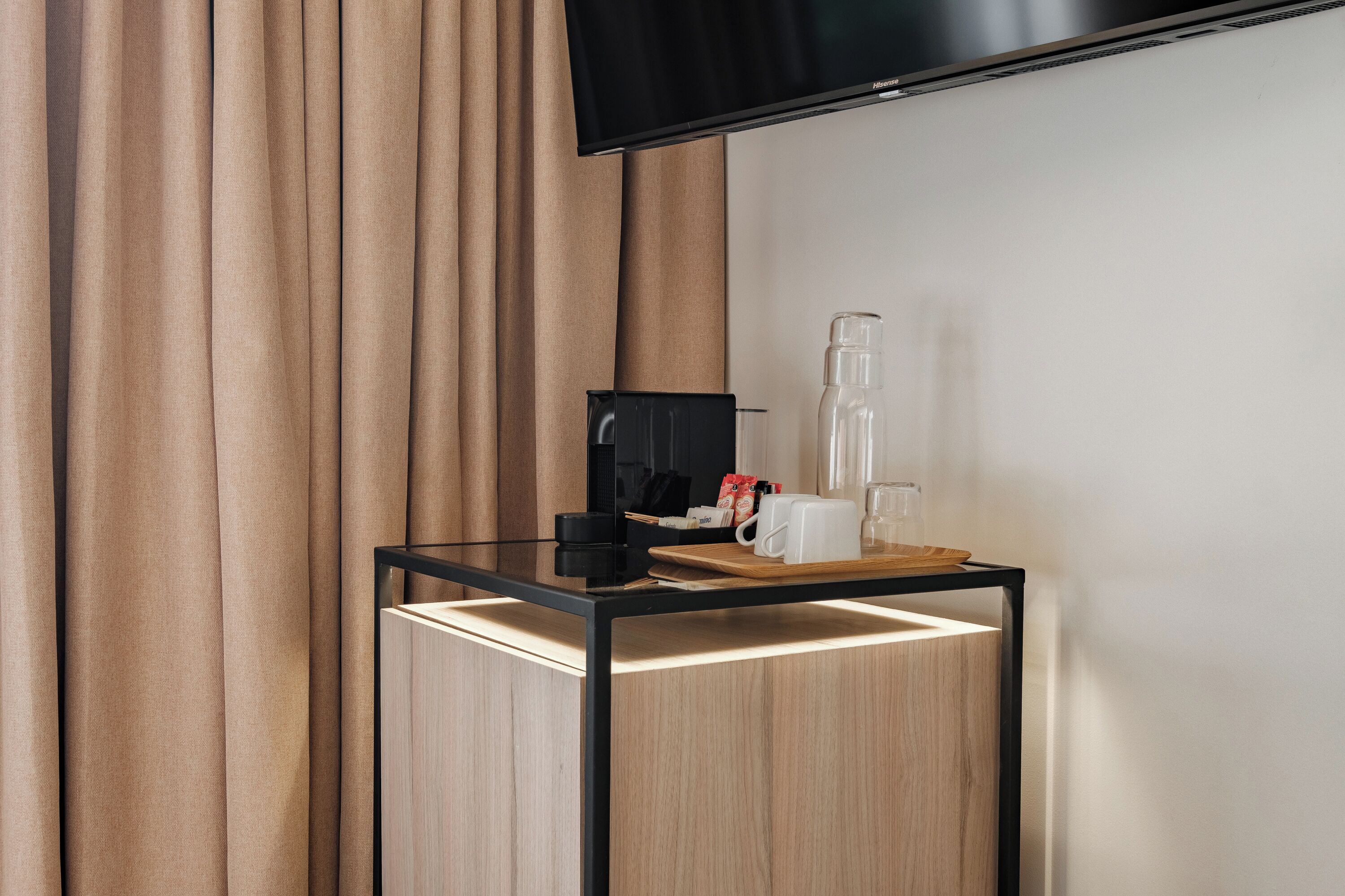 A modern hotel room with a glass table, a coffee maker, a mug, and a glass of water.
