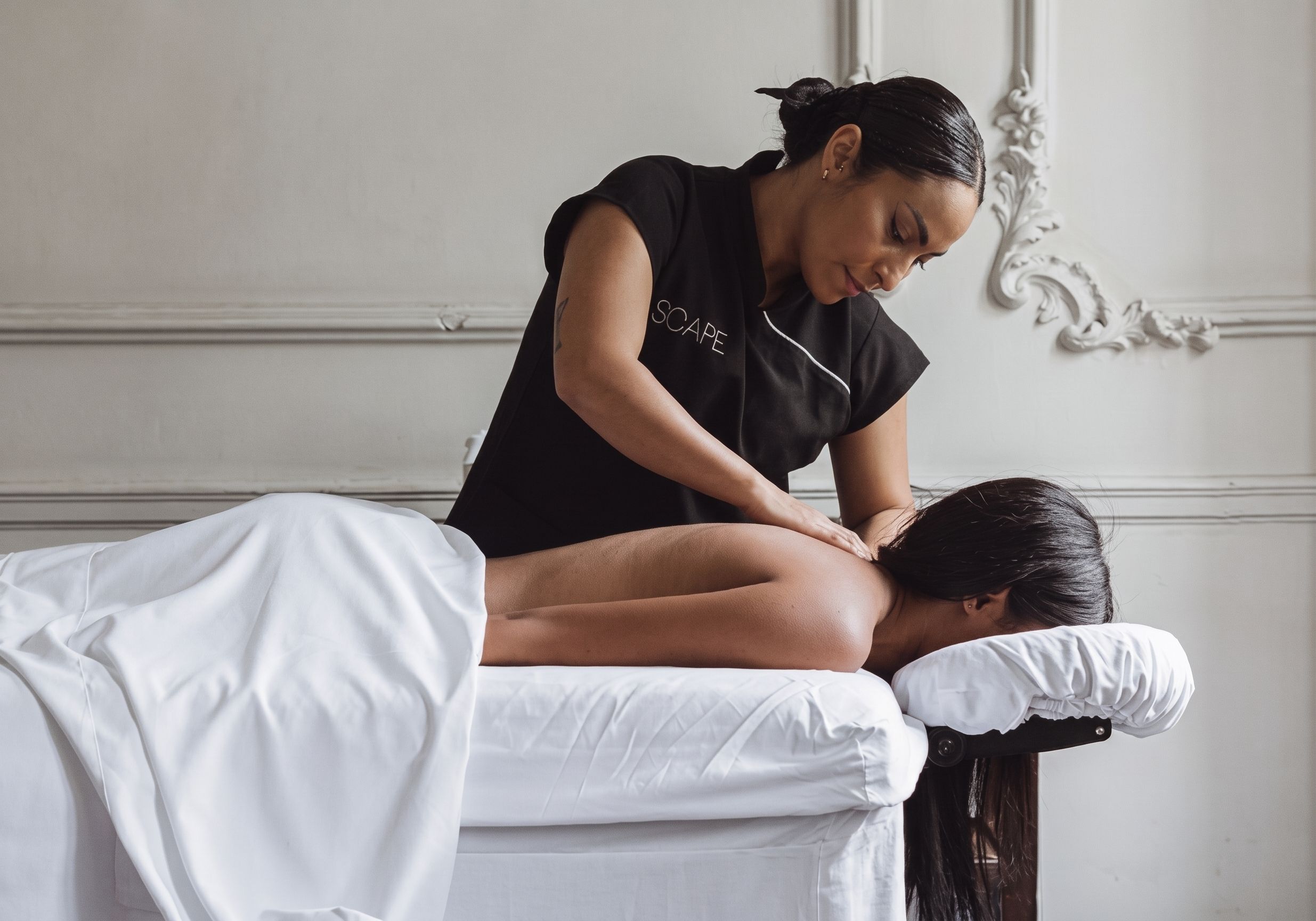 A person receiving a massage in a room with a white bed and ornate wall decorations.