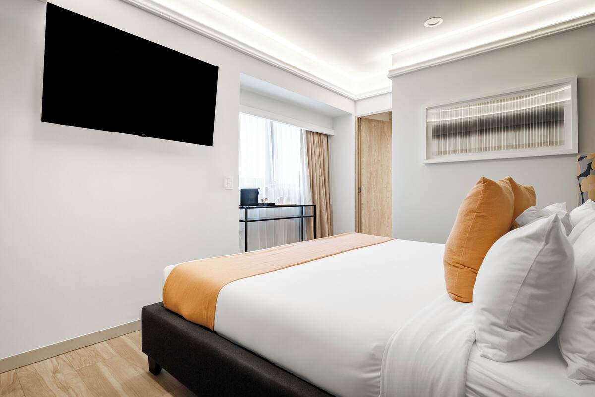 Een moderne hotelkamer met een groot bed, een flatscreen televisie aan de wand en een raam met gordijnen.