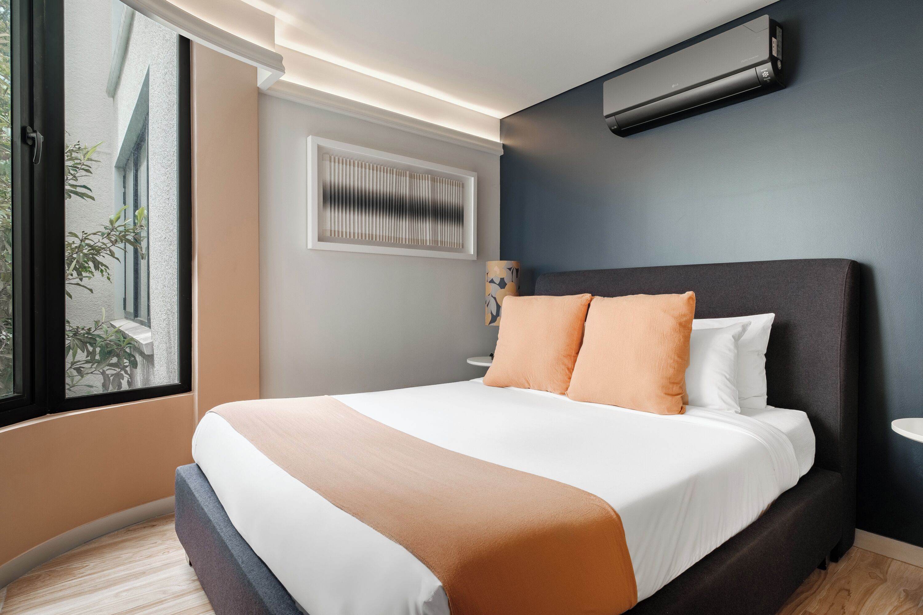 A modern bedroom with a large bed, a window, and an air conditioning unit.