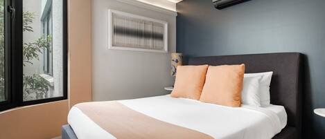 A modern bedroom with a large bed, a window, and an air conditioning unit.