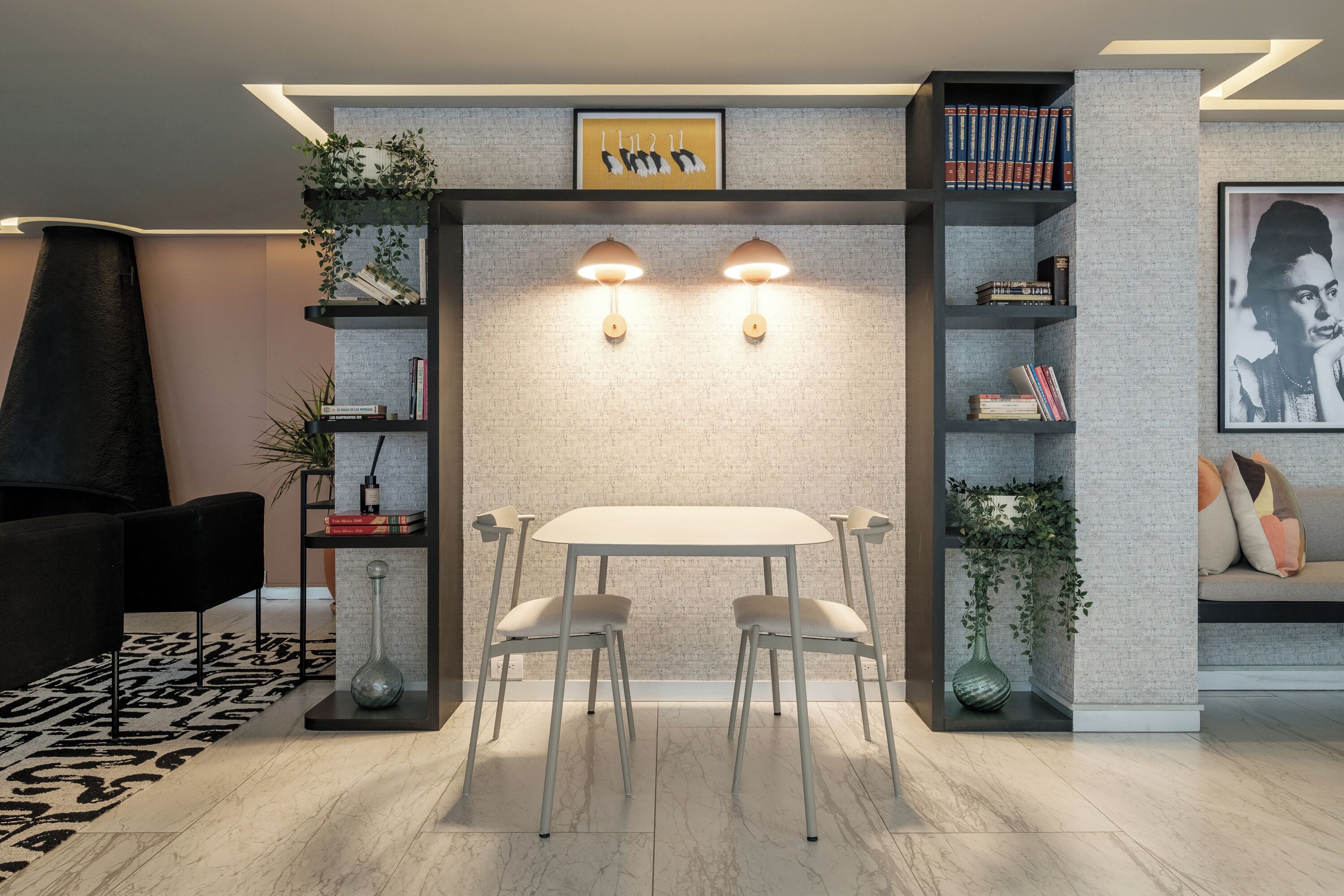 A modern dining area with a white table and chairs, surrounded by bookshelves and decorative plants.