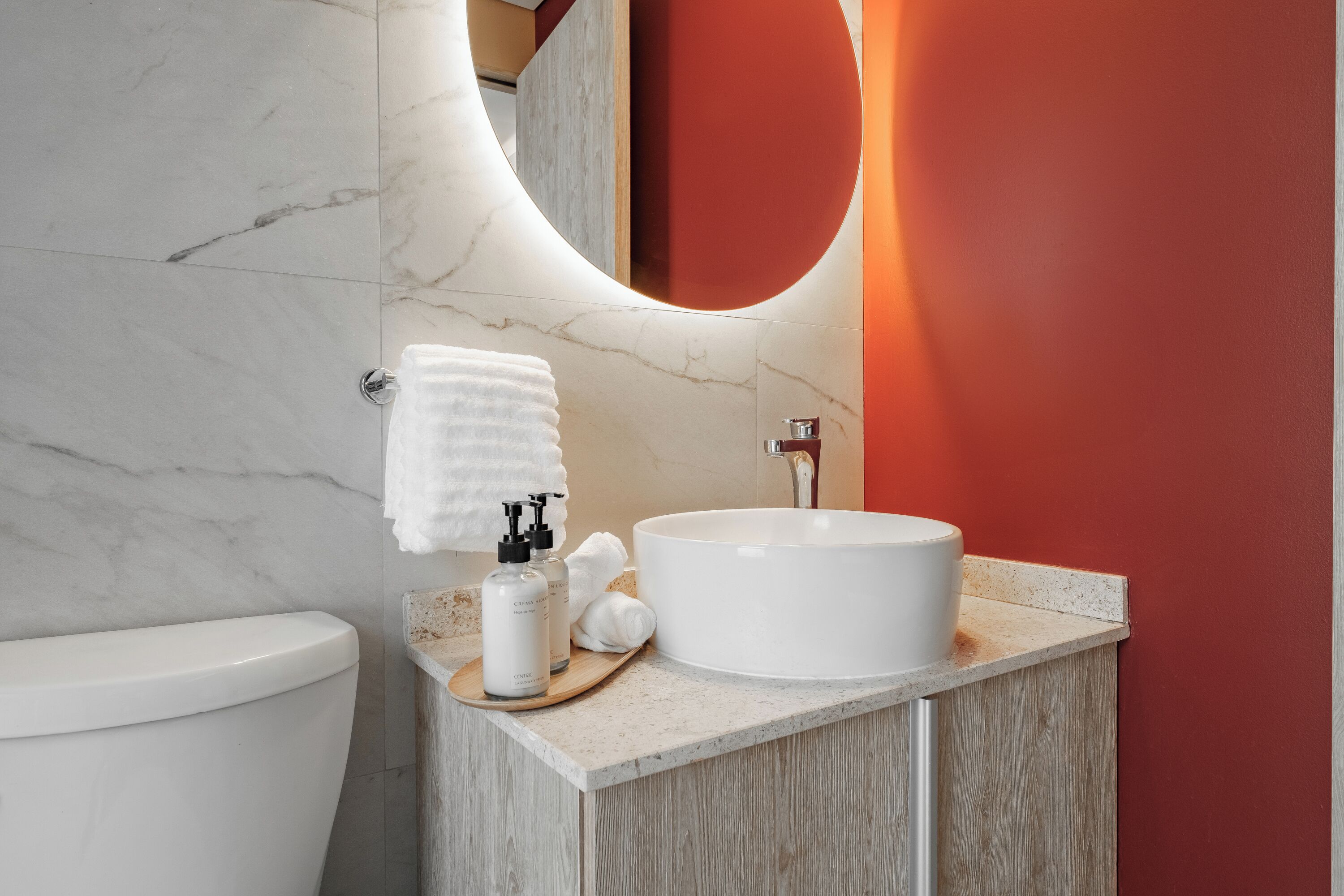 Un baño moderno con lavamanos blanco, paredes de mármol y tocador de madera.