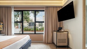 A modern hotel room with a large bed, a desk with a flat-screen TV, and a view of the outside.