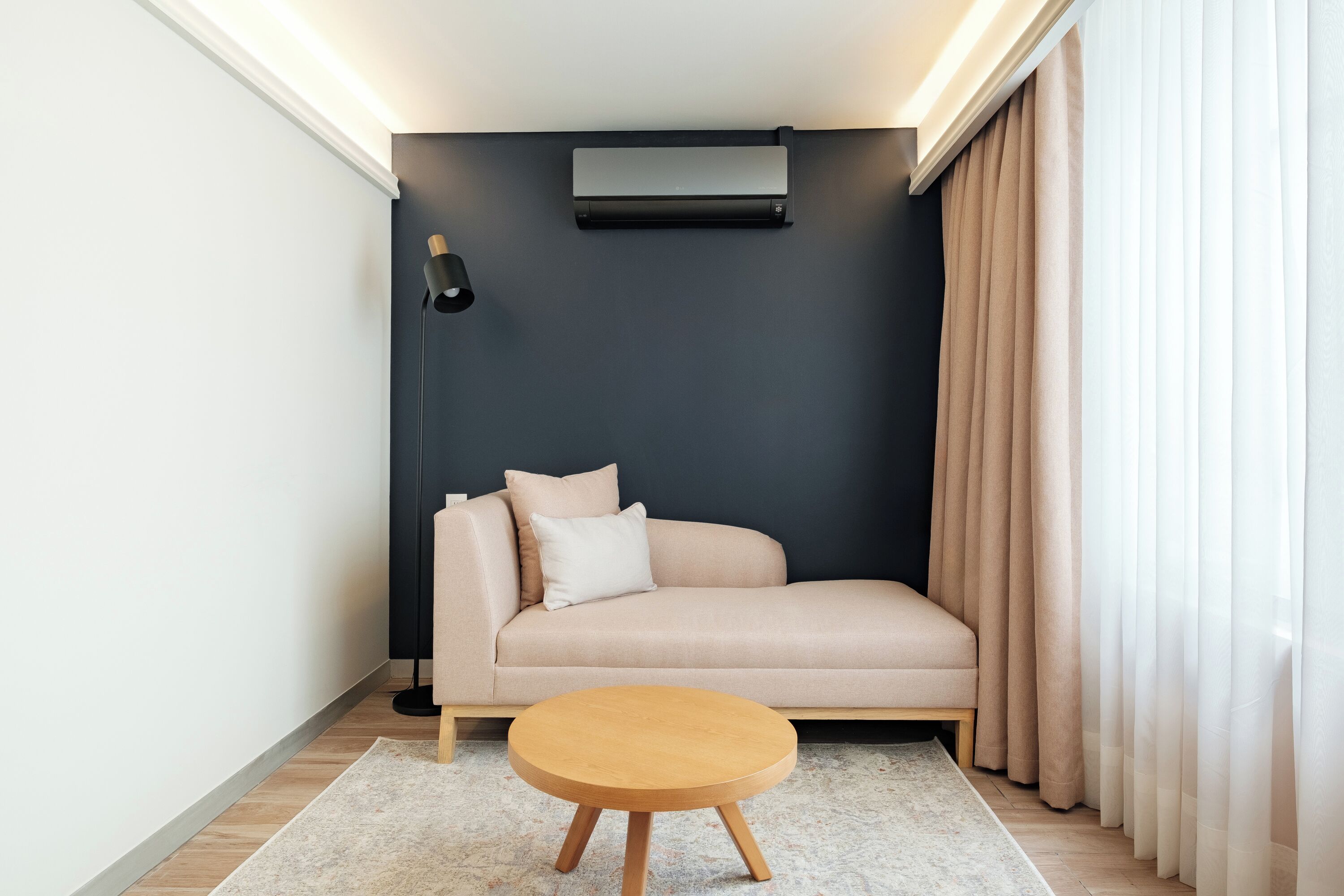 A modern living room with a beige sofa, a round wooden coffee table, a black floor lamp, and a wall-mounted air conditioner.