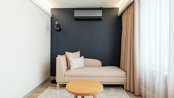 A modern living room with a beige sofa, a round wooden coffee table, a black floor lamp, and a wall-mounted air conditioner.
