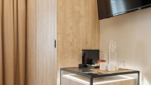 Una habitación de hotel moderna con un armario de madera, una mesa de centro de vidrio y un televisor de pantalla plana montado encima.