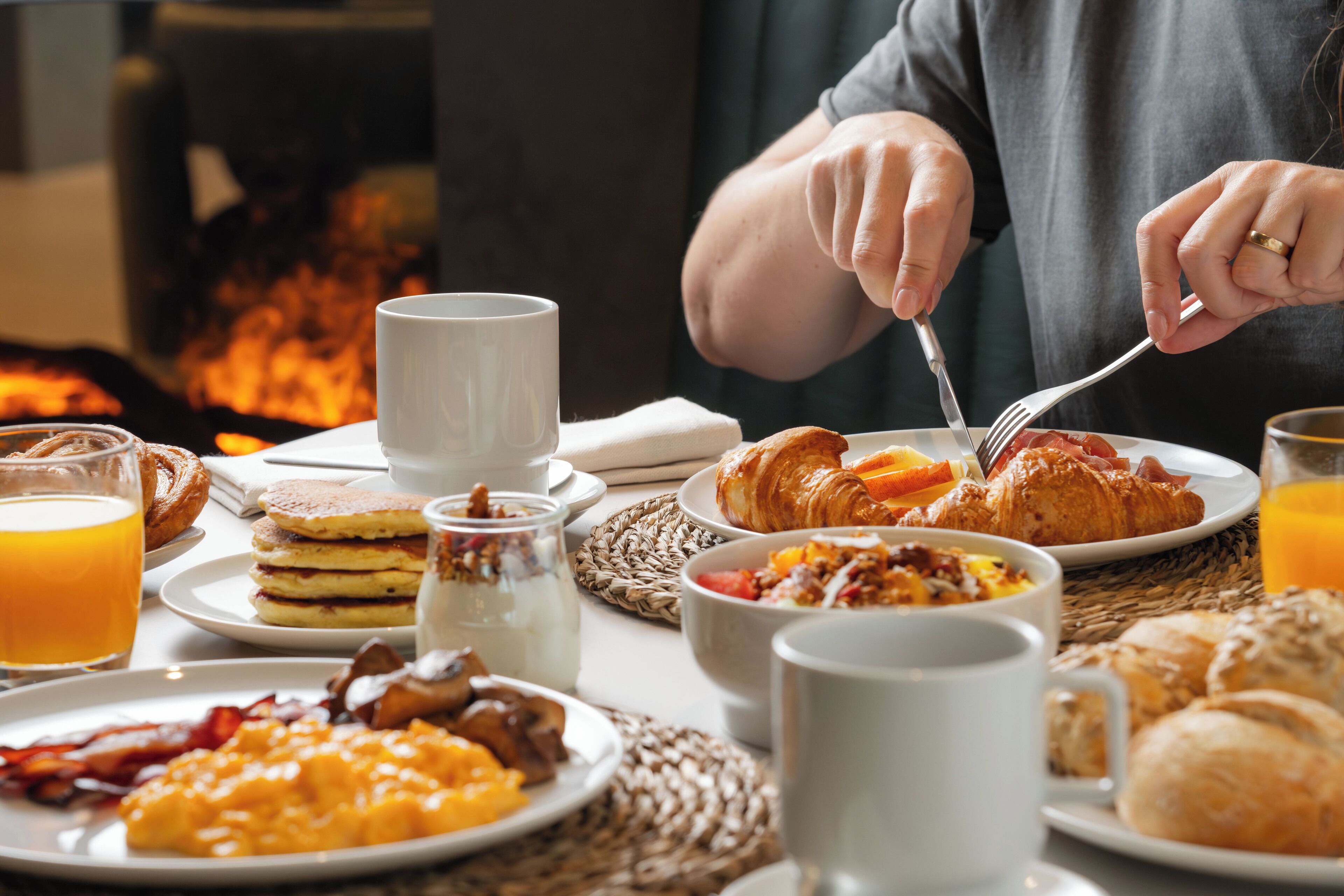 Una escena de desayuno con diferentes platos, como huevos, tocino y pasteles, sobre una mesa con un mantel tejido.