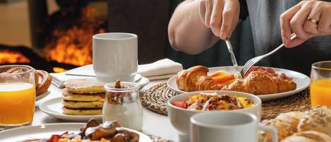 Una escena de desayuno con diferentes platos, como huevos, tocino y pasteles, sobre una mesa con un mantel tejido.