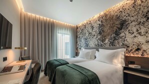 Hotelkamer met een groot bed, een bureau met lamp, een televisie en een wand met een structuur.