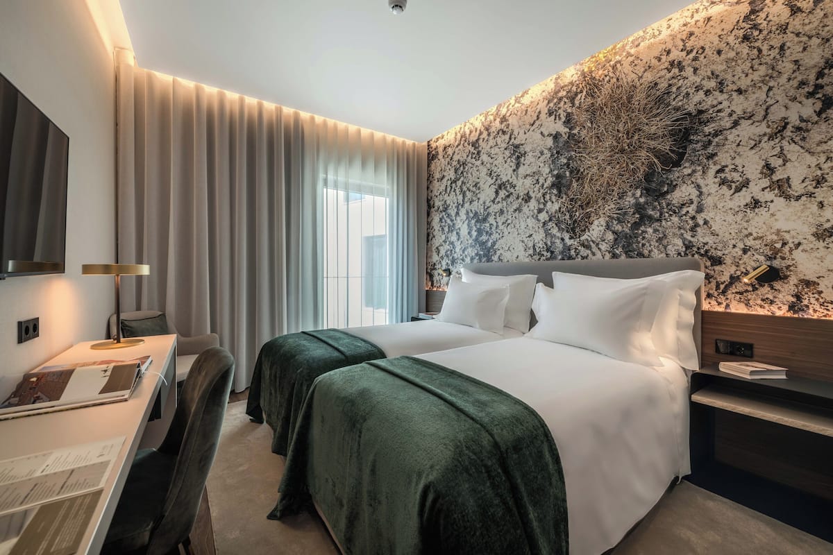 Ein Hotelzimmer mit einem großen Bett, einem Schreibtisch mit Lampe, einem Fernseher und einer Wand mit strukturierter Oberfläche.