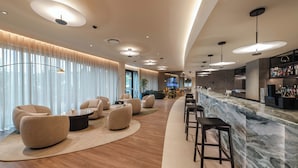 Een moderne bar met een marmeren aanrecht, barstoelen en een zithoek met ronde stoelen en een bijzettafeltje.