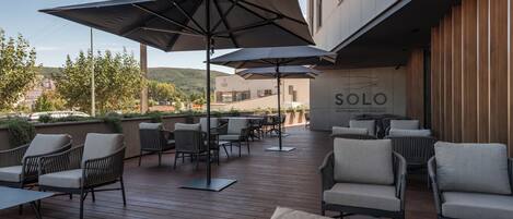An outdoor seating area with tables and chairs, umbrellas, and a building with a sign that reads "SOLO RESTAURANTE LOUNGE BAR".
