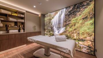 Um quarto de spa com um armário de madeira, uma mesa de massagem e um grande mural com uma cascata.