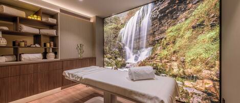 Um quarto de spa com um armário de madeira, uma mesa de massagem e um grande mural com uma cascata.
