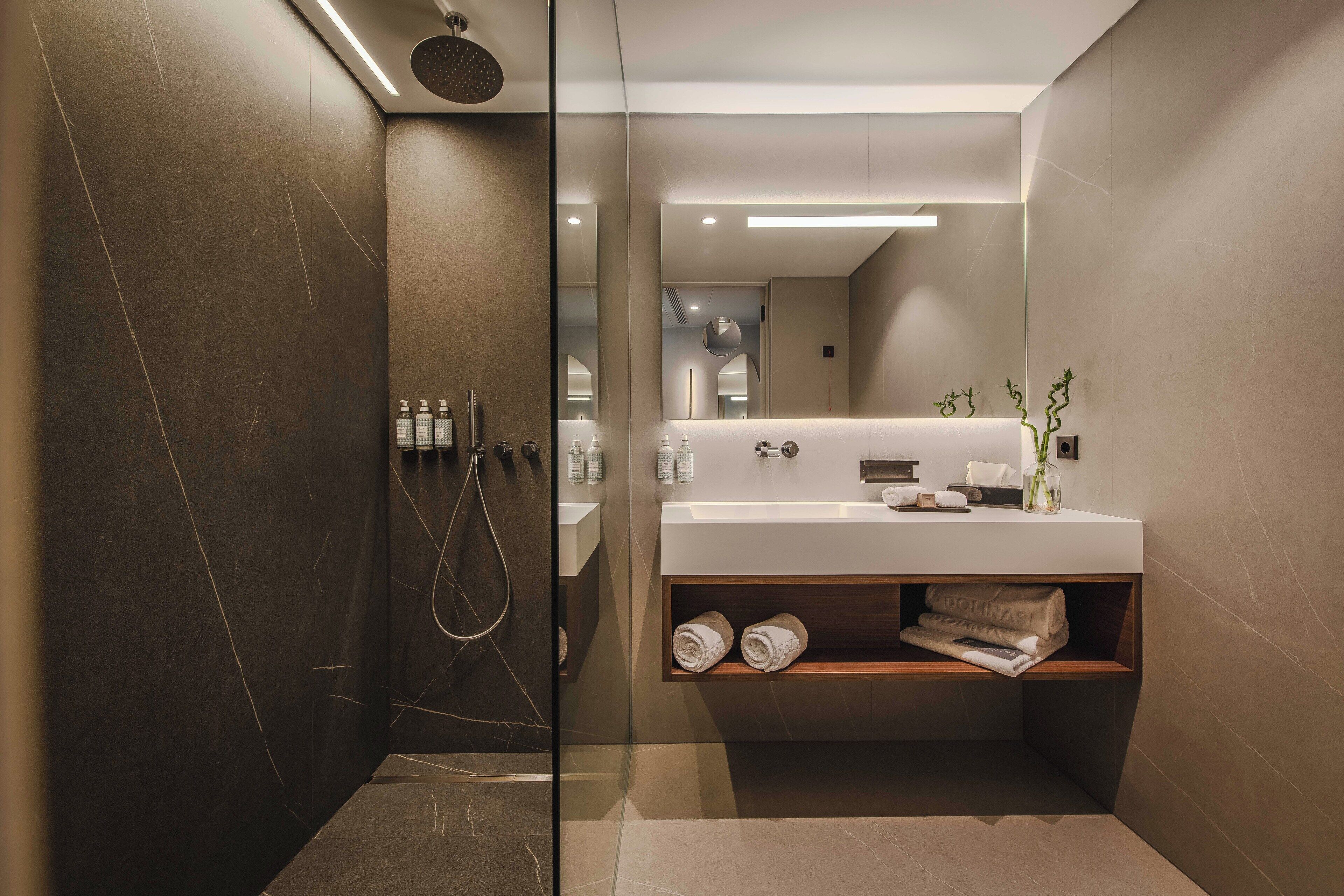 A modern bathroom with a glass-enclosed shower, a large mirror, and a built-in vanity with a wooden shelf.