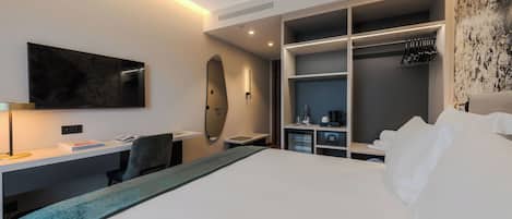 A modern hotel room with a large bed, a desk with a chair, a flat-screen TV, a wardrobe, and a mirror.