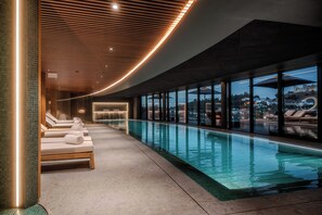 A modern indoor swimming pool with lounge chairs and a view of the cityscape. - Dolinas Climbing Hotel (Porto de Mos)