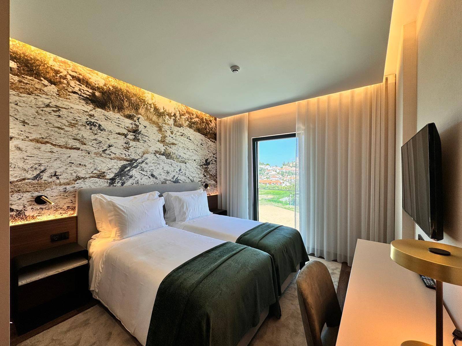 Une chambre d’hôtel avec un grand lit, un bureau, une télévision et une vue sur un paysage montagneux.