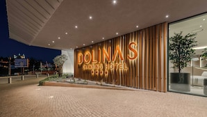 Het uiterlijk van het Dolinas Climbing Hotel, met een opvallend verlicht bord, een geplaveid entreegebied en een modern architectonisch ontwerp.