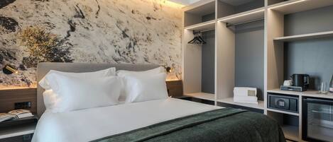 Una habitación de hotel moderna con una cama grande, una pared de mármol, un armario empotrado y una pequeña cocina.