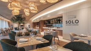 Een modern restaurant met een gebogen plafond, houten tafels en groene stoelen. Er staat een bord waarop te lezen is: SOLO Restaurant Lounge Bar.
