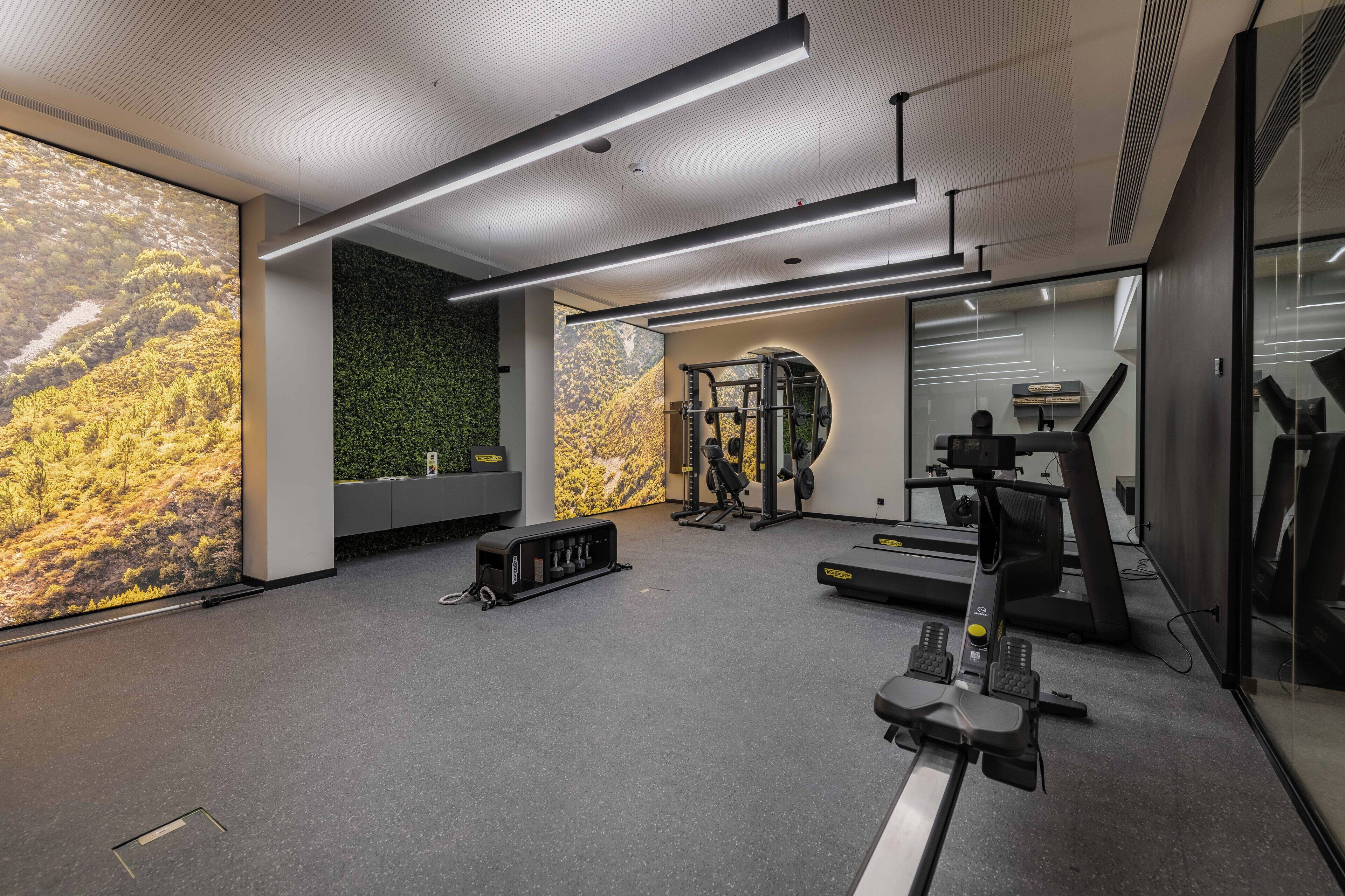 A modern gym with exercise equipment, a large wall-mounted screen, and a green wall accent.