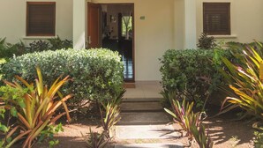 Un edificio con entrada central, el número '412' sobre la puerta y un pequeño jardín con diversas plantas al frente.