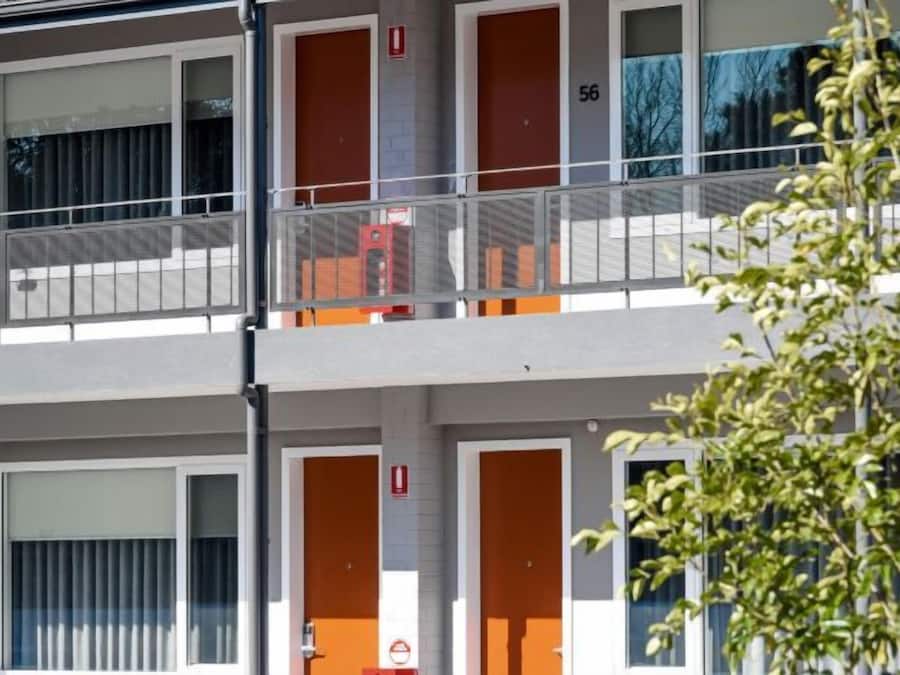 Un edifici de diversos pisos amb portes i finestres taronja, balcons i un tub d'incendis visible.