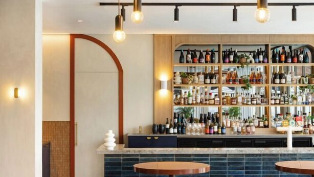 A bar area with multiple shelves of bottles, a counter, and three round tables with chairs. - HotelMOTEL Adelaide (Adelaide)