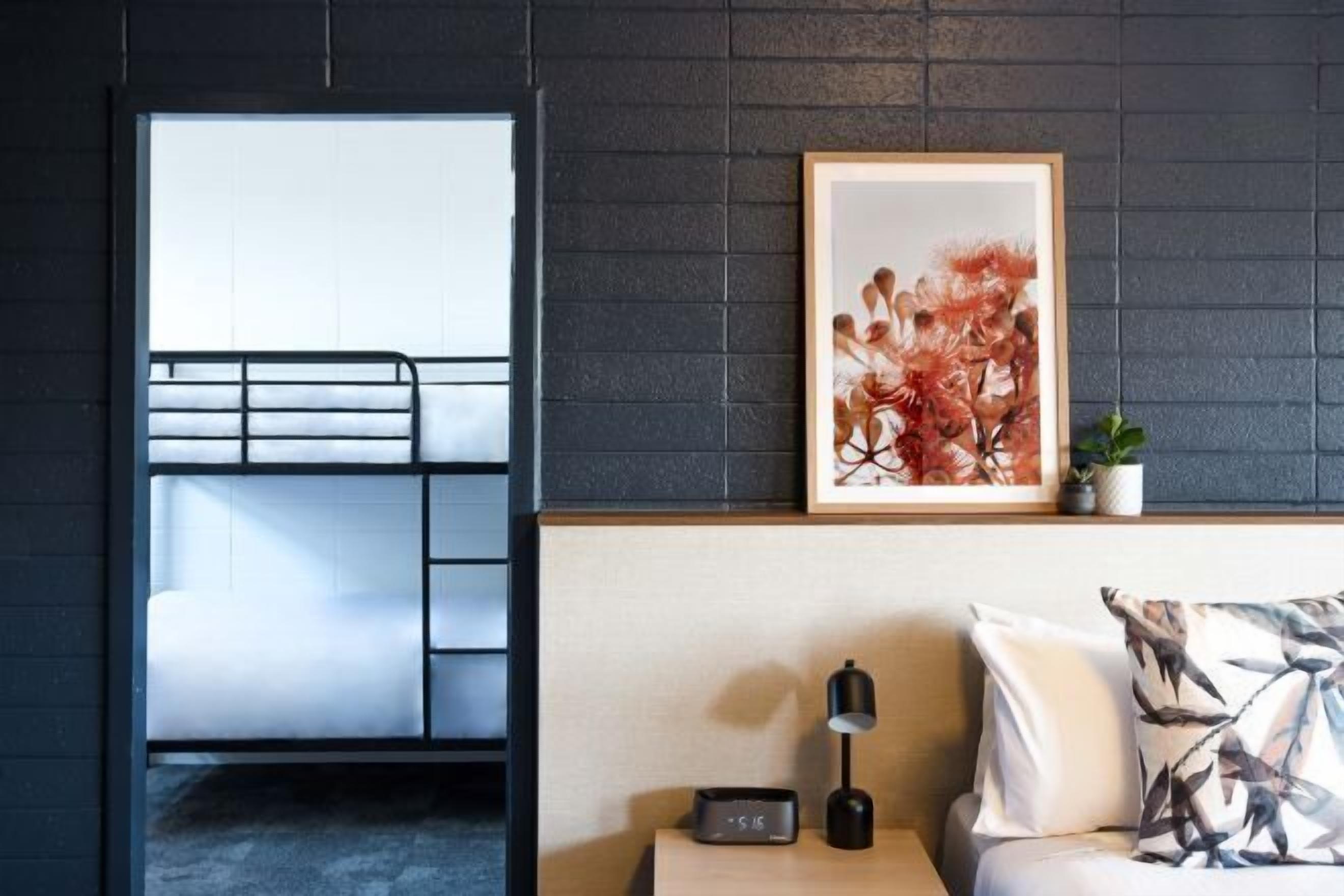 Une chambre avec un lit superposé, une table de chevet avec une lampe, une œuvre d’art encadrée et une petite plante.