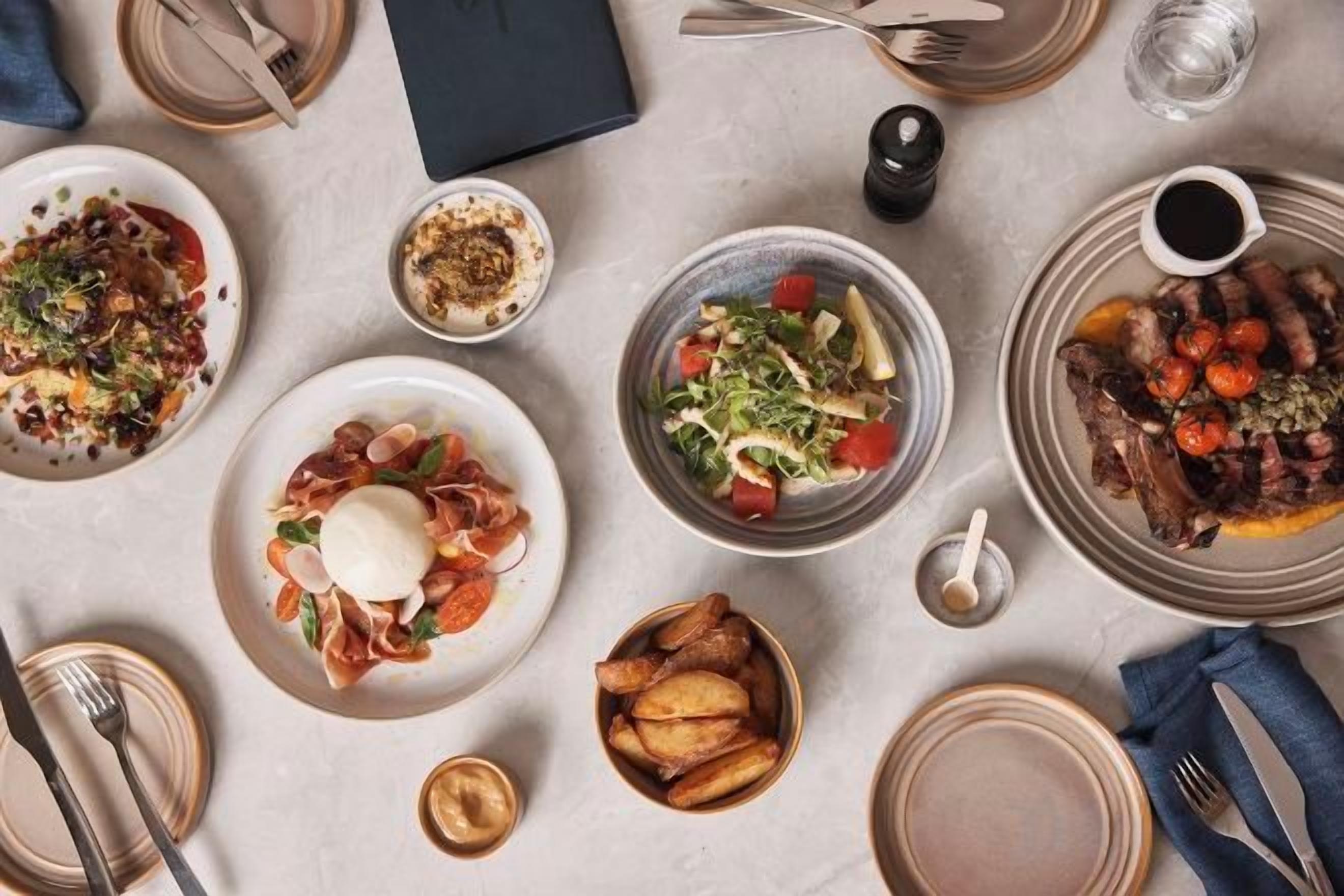 A dining table with various dishes, utensils, and a napkin.